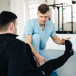 Kỹ thuật viên hỗ trợ người bệnh tập nâng chân trong phòng phục hồi
